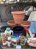 Overview of large pots, various fertilizers, weed preventer, and additional gardening products arranged on a table outdoors.