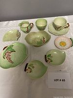 Full view of all ceramic pieces together arranged on a white surface showing teacup, saucer, cream pitcher, sugar bowl and assorted leaf-shaped dishes including a daisy plate.
