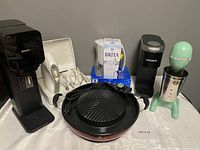 Photo showing the full lot with Nutrigrill, Brita water filter, Keurig coffee maker, Sodastream machine, Hamilton Beach drink mixer, and GE handheld mixer with attachments in case.