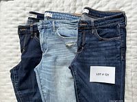 Three pairs of Abercrombie + Fitch ladies jeans laid flat on a white textured surface, showing the front sides, size tags visible as 28.