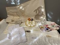 Full view of linens including Easter table runner with bunny designs, white placemats, embroidered napkins, floral napkins, vintage egg plate, Pysanky eggs, and napkin rings.