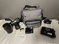 All items displayed: camera body with lens, flashes, lens case, small film cylinder, and camera bag.