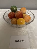 Full view of crystal bowl with multiple polished onyx fruit arranged inside on patterned tablecloth.