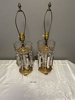 Full view of both brass and crystal lamps on table showing structure, finials, and crystal details.