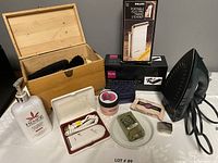 Overview photo of the lot showing the Proctor Silex iron, wooden shoe polish box with brushes, Philips Lady Shave in travel case, Hempz lotion, jar of cream, soap bars, and boxed Philips clothes steamer.