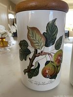 Close-up of large white ceramic canister decorated with fig illustration and wood lid