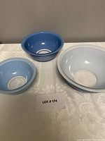 Set of nine Pyrex nesting bowls arranged on a cloth with lot card. Bowls are shown stacked and spaced individually to show the different colors and sizes.