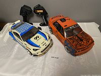 Both 12-inch remote control cars side by side with their respective controllers placed behind them on a white cloth.