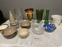 Front and full view of assorted vases, bowls, and flowerpots arranged on cloth surface showing all items.