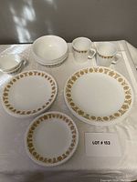 Overview of plates, bowls, and Pyrex mugs all with gold butterfly floral patterns on white glass.