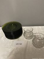 Stack of twelve green glass snack plates with thumbprint pattern and two clear glass creamers on the side