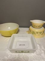 Photo displaying yellow Pyrex mixing bowl with solid color and a square white frosted Glasbake casserole dish with delicate green floral pattern.