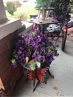 Front view of metal butterfly side table with faux purple flowers on top and wooden display table beside it.