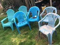 Photo of six plastic outdoor stacking chairs on a grassy area, three light blue Adirondack style and three light gray slatted style showing dirt and wear.