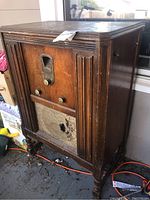 Front view of the antique Majestic radio cabinet showing wooden finish, front dial, knobs, speaker cover with holes, and carved details.