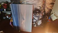 Photo showing mountain landscape canvas leaning against larger Albert Einstein canvas with some surrounding items.