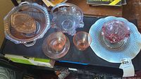 Overview photo showing all glassware items including pink Depression glass plates, cups, milk glass bowl, and ruffled pink bowl.