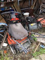 Lawnmowers arranged outdoors in a shed with dirt and garden items around.
