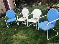 Four metal outdoor chairs on grass, two blue and two white. White tubular frames with visible dirt and rust spots.