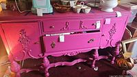 Bright pink painted wooden server with carved decorative details and open drawer showing interior storage.