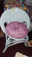 Full view of the child's white wicker chair with a round pink velvet cushion placed on the seat showing the chair structure and cushion design.
