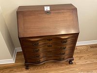 Front view of closed drop-front desk showing serpentine drawer fronts and brass bail handles