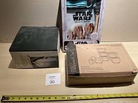Front view of unopened Pampered Chef covered vegetable dish in original box next to Pampered Chef prep bowls in cardboard packaging and Star Wars Galactic Baking box.