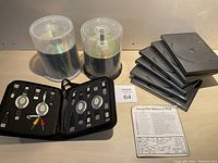 Wide view of two spindle stacks of DVD-R discs, six black DVD cases stacked, zippered kit with multiple retractable cables and plugs, plus a printed sheet titled 'Computer Universal Bag'