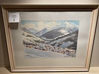Framed watercolor painting showing a snowy European village with mountains in the background, with matting and a wooden frame.