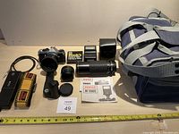 Pentax ME Super 35mm film camera package items spread on table including camera body, flash, case, 70-300mm zoom lens, 2x converter, shutter release cable, shoulder strap, power winder, carrying case, user guides, Kodak 110 camera.