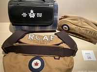 Three items displayed: RCAF Airman's Kit shoulder bag, smaller zippered bag, and folded car blanket in black carrying case with RCAF Officers' Mess insignia.