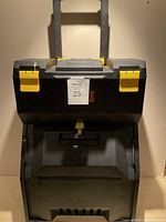 Front view of Stanley rolling tool carrier showing black plastic body with yellow latch clasps and handle.