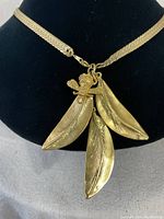 Front view of the necklace showing the bee and three leaf pendants on a black display stand.