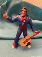 Front view of Elvis Presley rubber figurine in blue jumpsuit holding a guitar, showing details of costume and facial features.