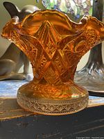 Front side view of ruffled marigold carnival glass punch bowl showing ornate pressed pattern and scalloped edge.