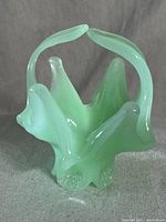 Front view of mini jadeite candy bowl showing ruffled edges and curved handle arching over the bowl