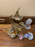 Five mixed glass sculptures displayed on a wooden ledge including colorful bird, clear abstract piece, two small glass items, and frosted owl.