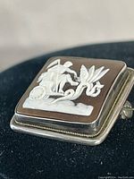 Close-up side angle showing the detailed relief of a man in chariot with serpent and the sterling silver frame with twisted rope border.