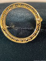 Top-down view of the round gold brooch showing filigree pattern and pin details