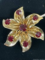 Front view of the three-dimensional gold-tone flower brooch with six prong-set red rhinestones.