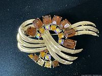 Front view of brooch showing faceted amber and smaller accent stones in gold-tone textured metal setting.