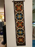 Full front view of the vertical rectangular wall hanging showing all four floral sections and the dark border as well as the hanging rod.