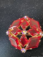 Close-up of front of vintage brooch showing red faceted stones and pink rhinestone accents in gold-tone metal setting