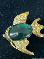 Close-up image of gold-tone angel fish brooch with green glass cabochon and small clear rhinestones on fins and tail.