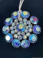 Top view of the round brooch showing large blue faceted rhinestones surrounding smaller clear and iridescent rhinestones.