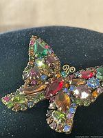 Close-up view of butterfly brooch showing multi-colored stones and brass setting.