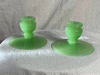 Front view of two jadeite green glass candle holders standing side by side on a neutral fabric background.