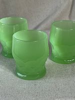 Three vintage Fenton jadeite juice cups displayed from the front, showing their smooth opaque green glass and shape.