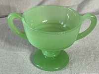 Front angle view of the pale green jadeite sugar cup with two handles and ribbed pedestal base.