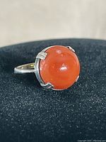 Close-up front view of vintage sterling silver ring with round orange stone mounted in four-prong setting.
